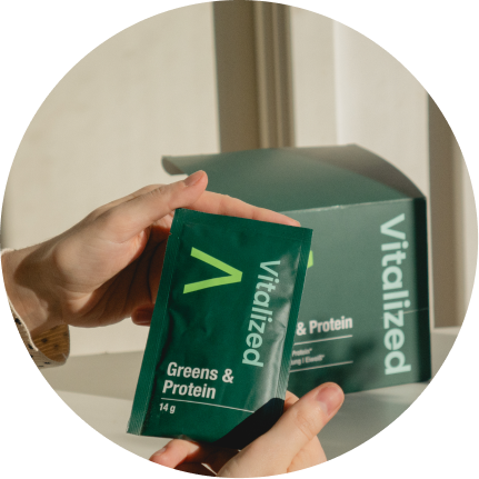 alt="Mano che tiene una bustina di Vitalized Greens & Protein in polvere davanti alla scatola»