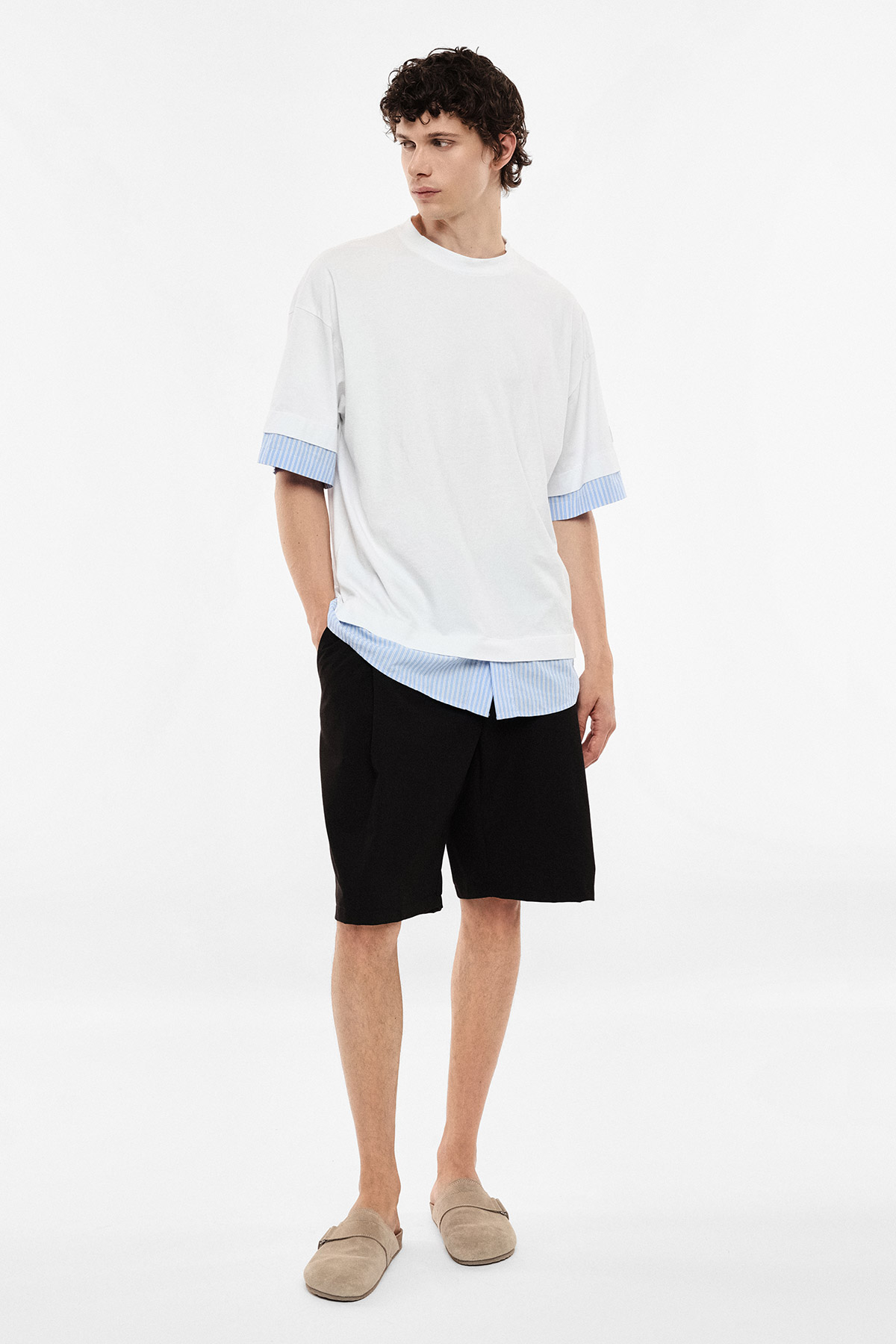 Male model wearing white oversized T-shirt with blue striped cuffs and hem, black shorts and beige loafers