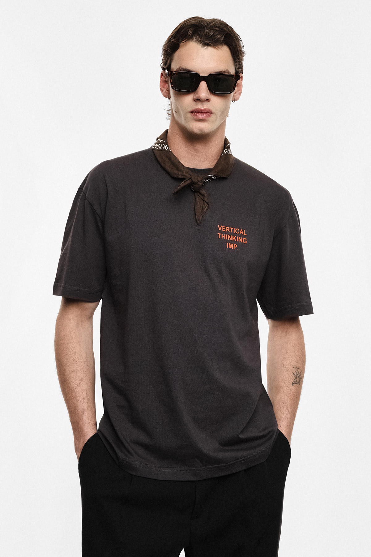 Model wearing dark grey t-shirt reading 'Vertical Thinking', brown bandana and black sunglasses, hands in pockets