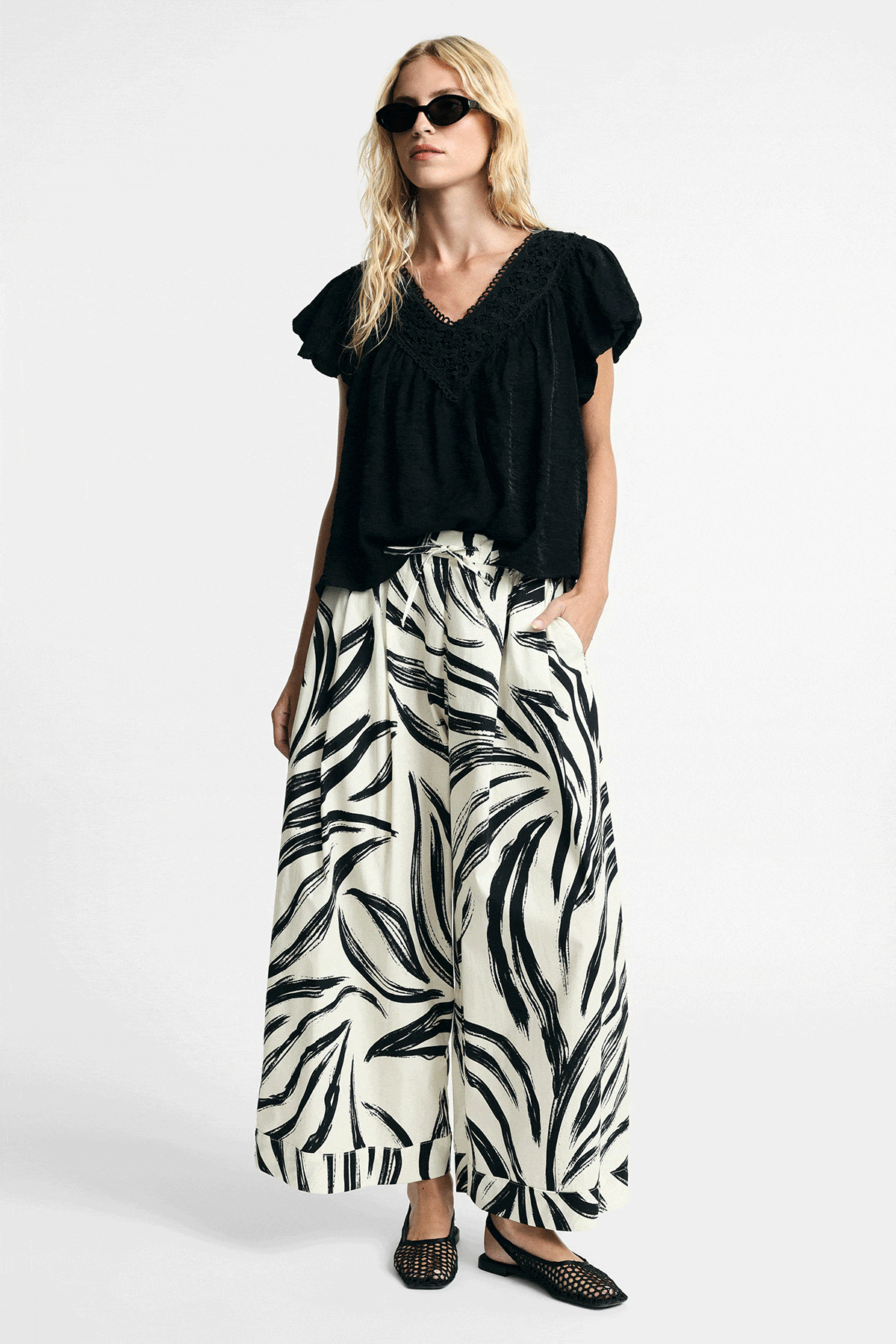Woman modelling black-and-white zebra-print wide-leg trousers with black short-sleeve blouse and flat sandals, front and back views