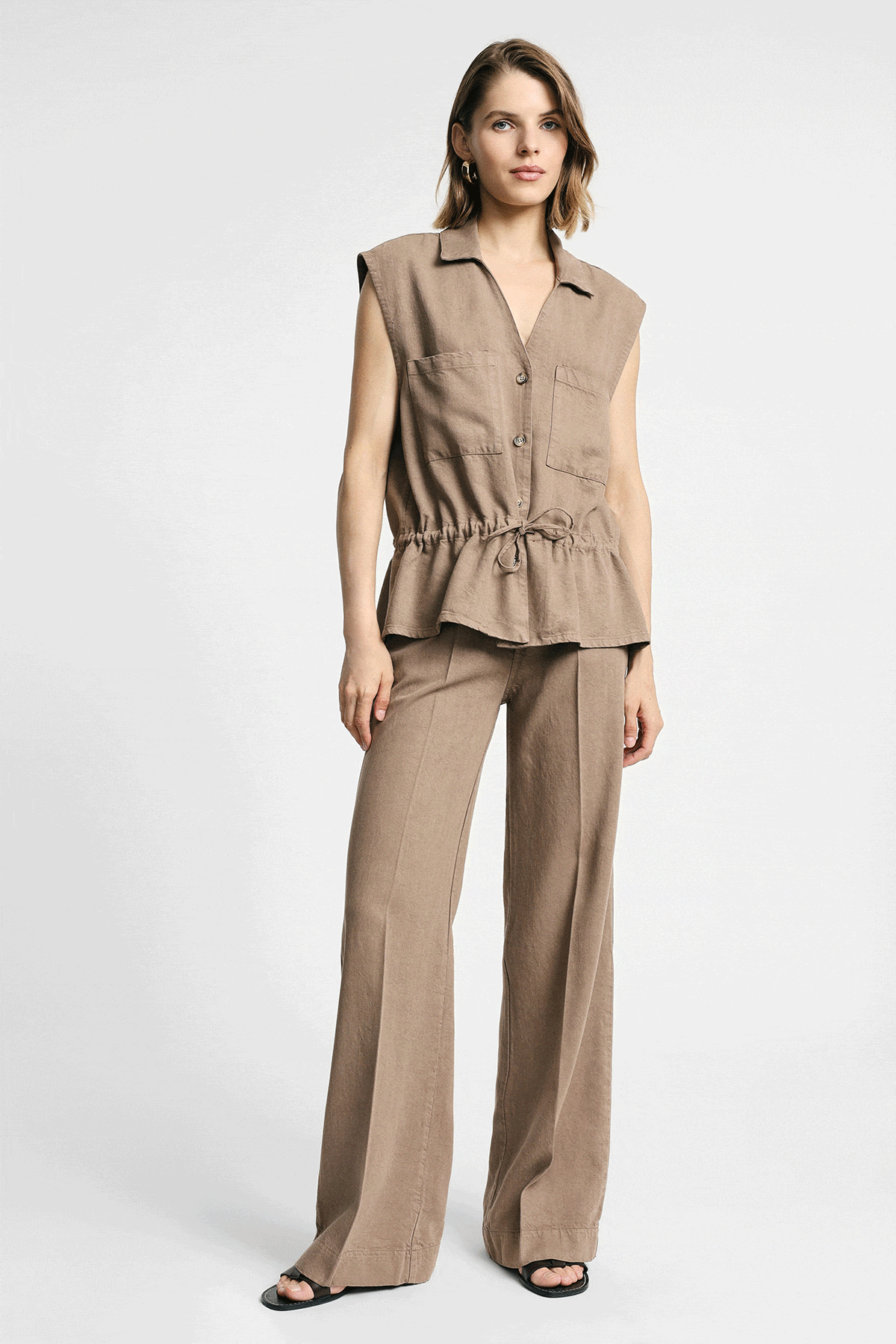 Model wearing beige sleeveless buttoned top with drawstring waist and matching wide-leg trousers, three poses on white background