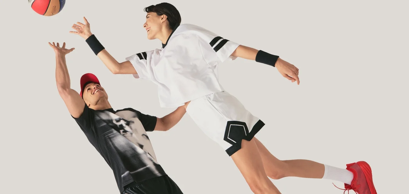 Due giocatori di basket a mezz'aria che cercano di prendere la palla, indossando abbigliamento sportivo nero e bianco su uno sfondo neutro.