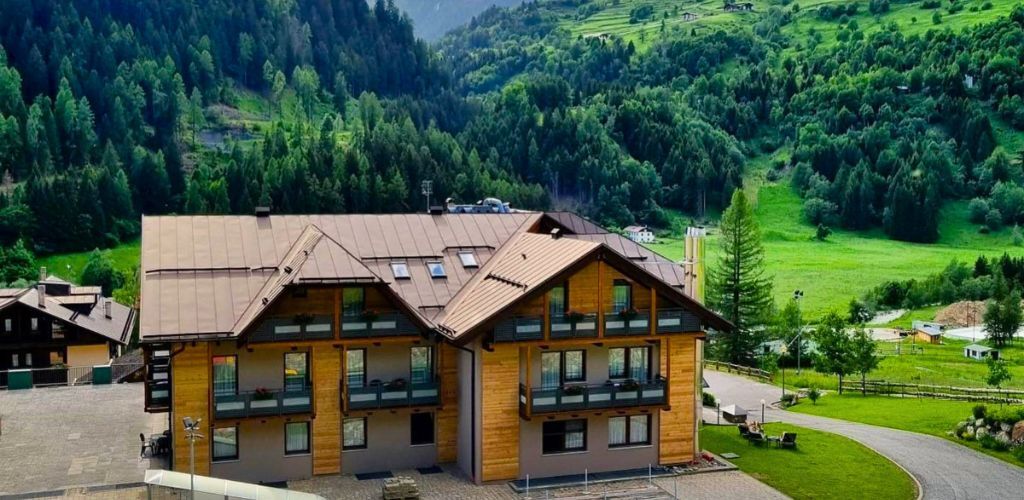 Wooden alpine chalet hotel with balconies set in green mountain valley near conifer forest and rolling meadows