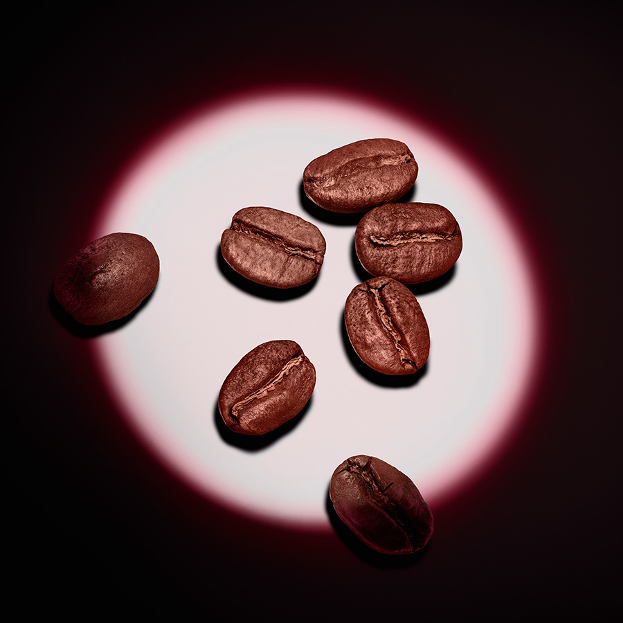 Sei chicchi di caff&egrave; tostato illuminati da un riflettore circolare su sfondo nero.