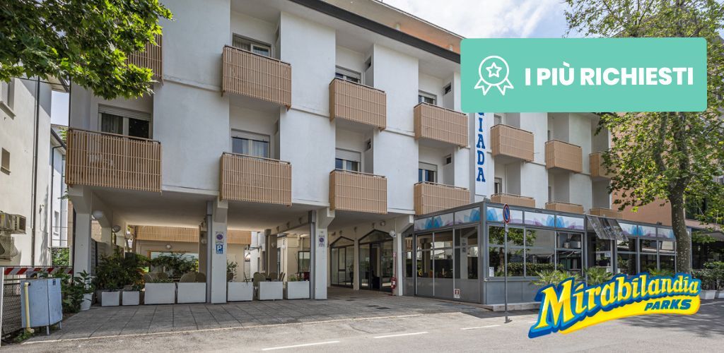 Exterior of a modern three-storey hotel with balcony rooms, covered entrance and Mirabilandia Parks sign, tree-lined street.
