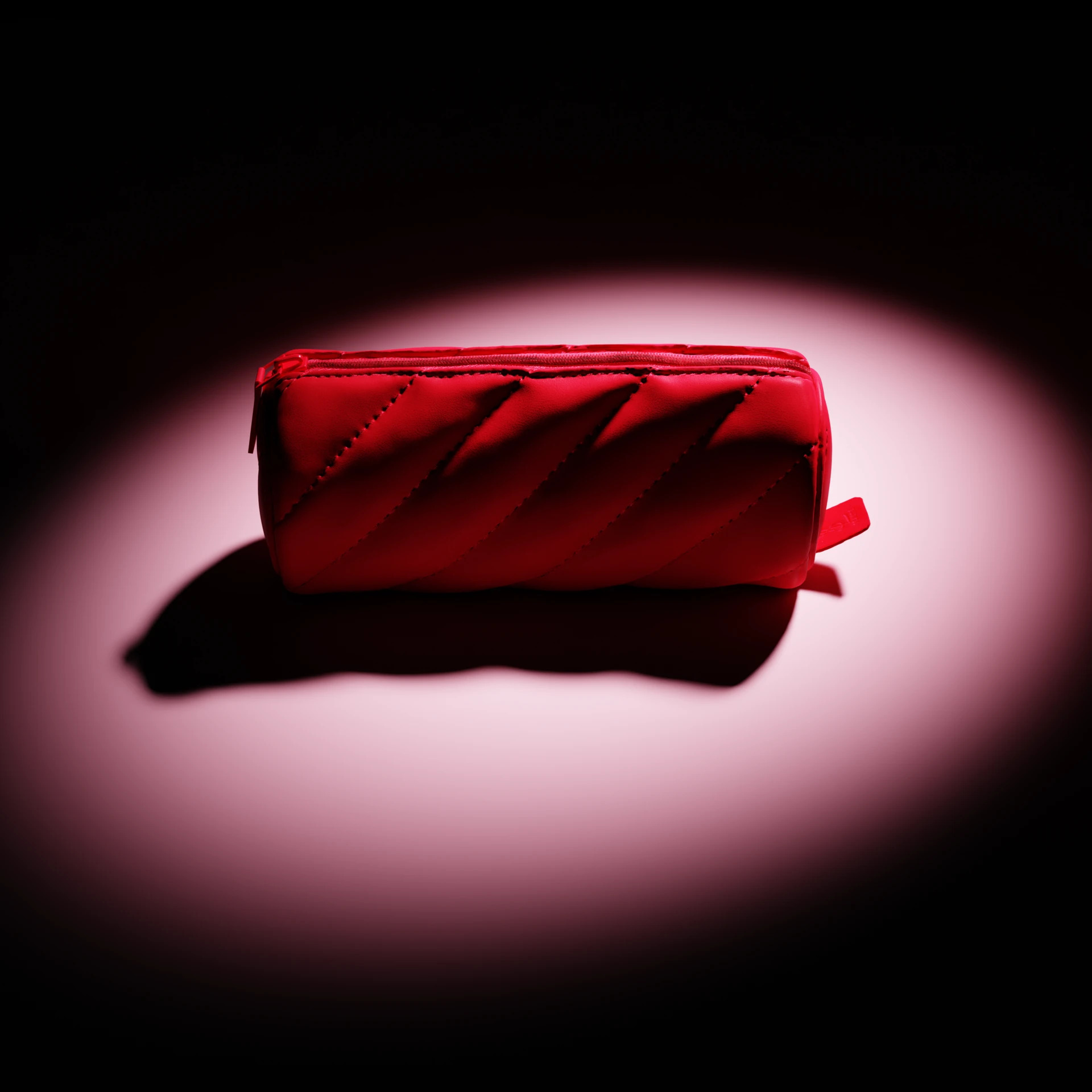 Una trousse da trucco cilindrica e trapuntata di un rosso brillante, illuminata da un riflettore centrale su sfondo scuro.
