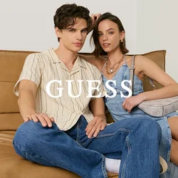 Giovane uomo con camicia a righe e jeans e giovane donna con vestito blu e tacchi neri seduti su un divano in pelle color cuoio contro uno sfondo semplice.