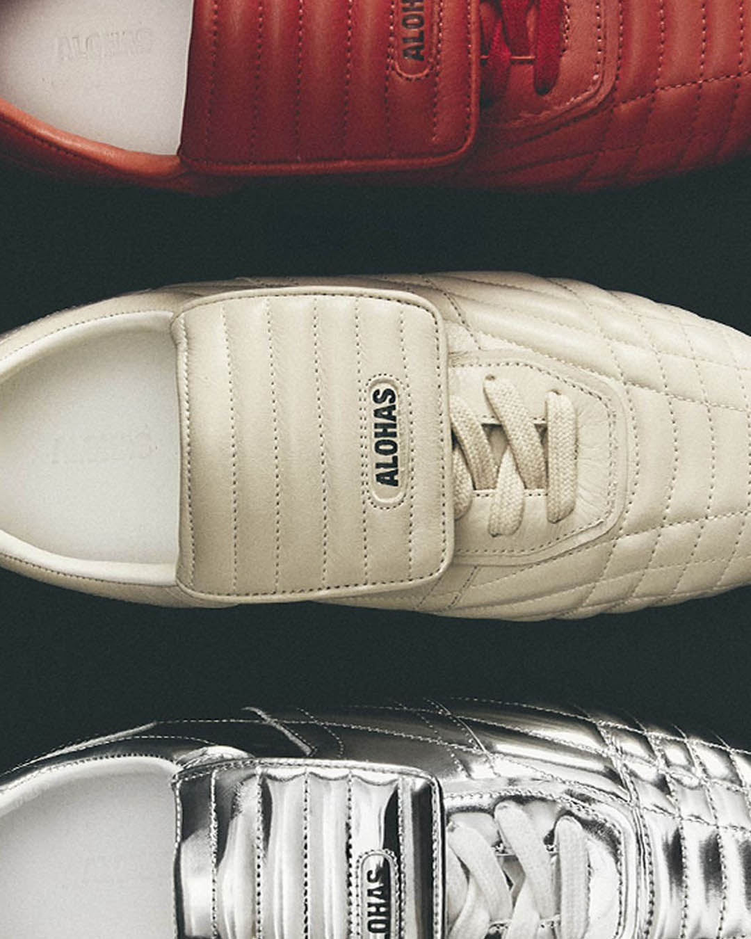 Top-down view of three ALOHAS quilted trainers in red, cream and metallic silver arranged vertically on a dark background