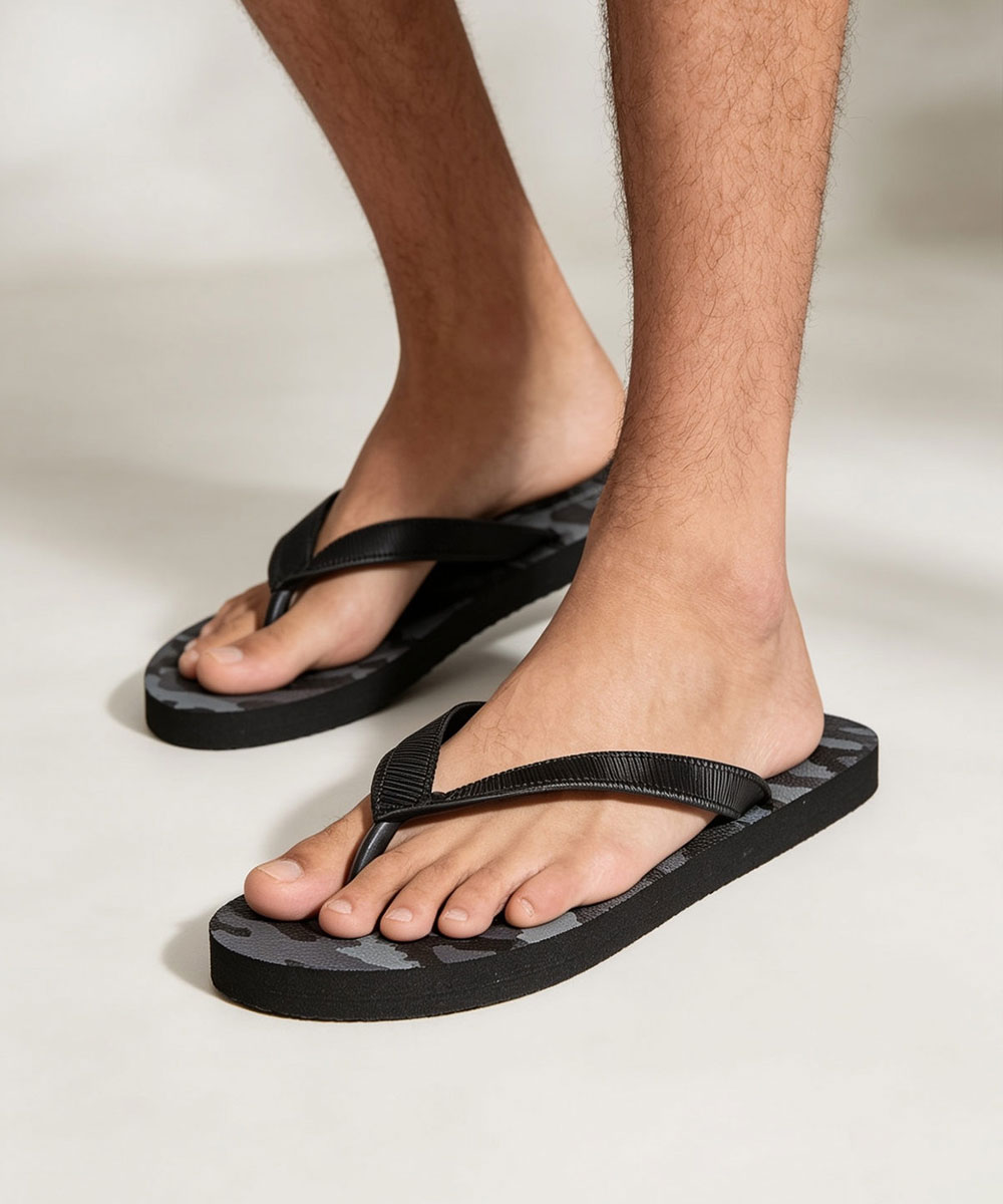 Close-up of bare male feet wearing black flip-flops with grey camouflage footbed on neutral background