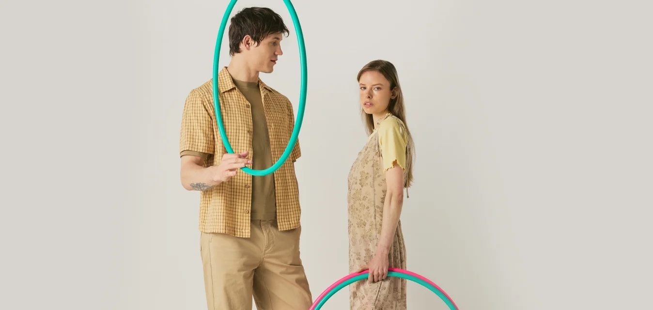 Un uomo e una donna stanno in piedi tenendo cerchi hula colorati; lui tiene un cerchio turchese vicino al viso, lei tiene due cerchi di fianco.