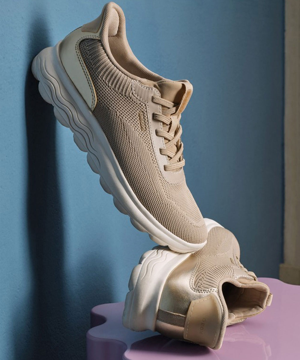 Beige knit lightweight trainers with chunky white soles, laced athletic shoes displayed on a blue background