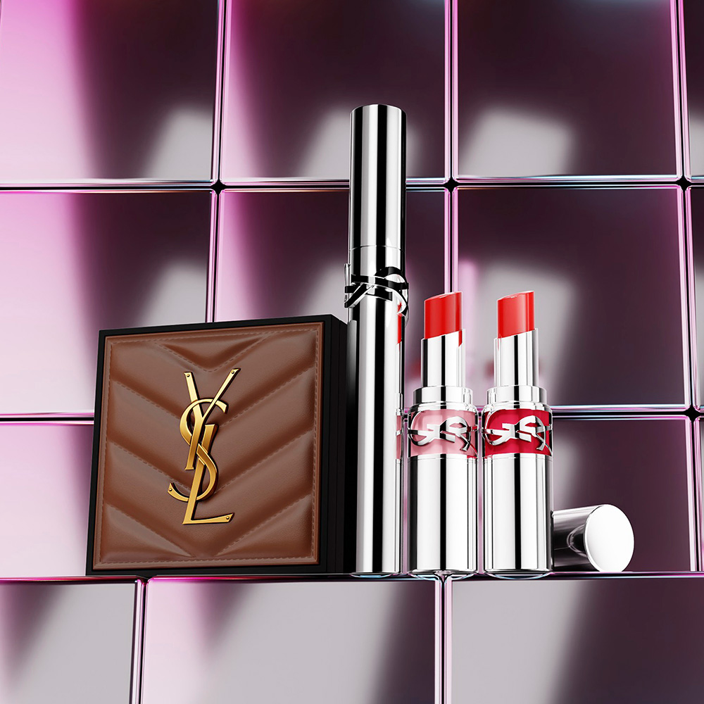 Una custodia in pelle marrone trapuntata YSL, un mascara e due rossetti esposti su uno sfondo di piastrelle metalliche.