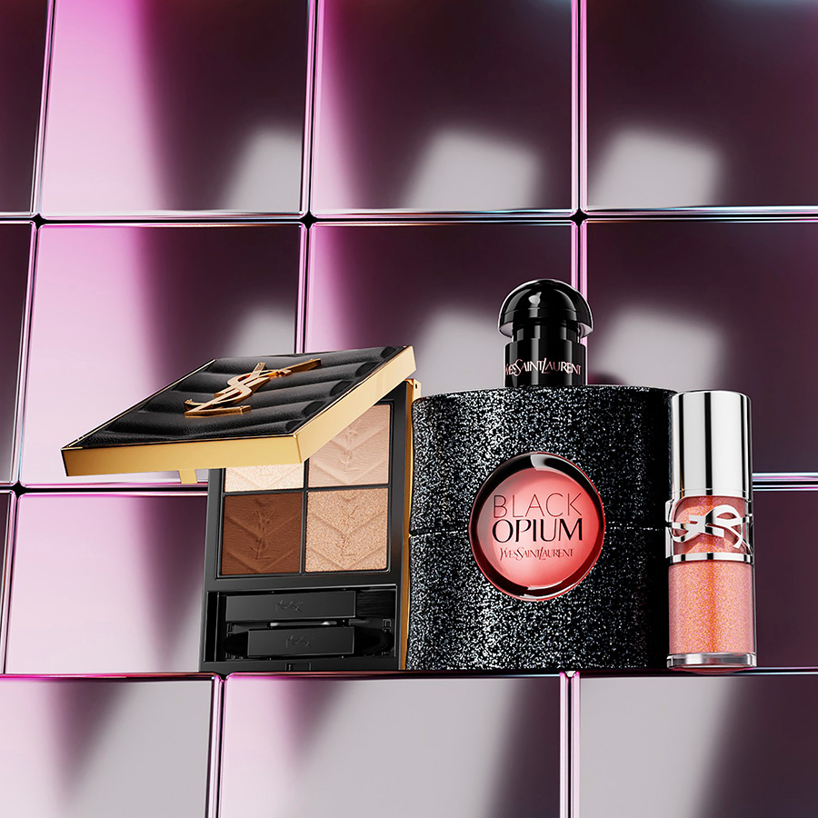 Una palette occhi, un flacone glitterato di profumo Black Opium e un gloss disposti su uno sfondo di piastrelle metalliche lucide.
