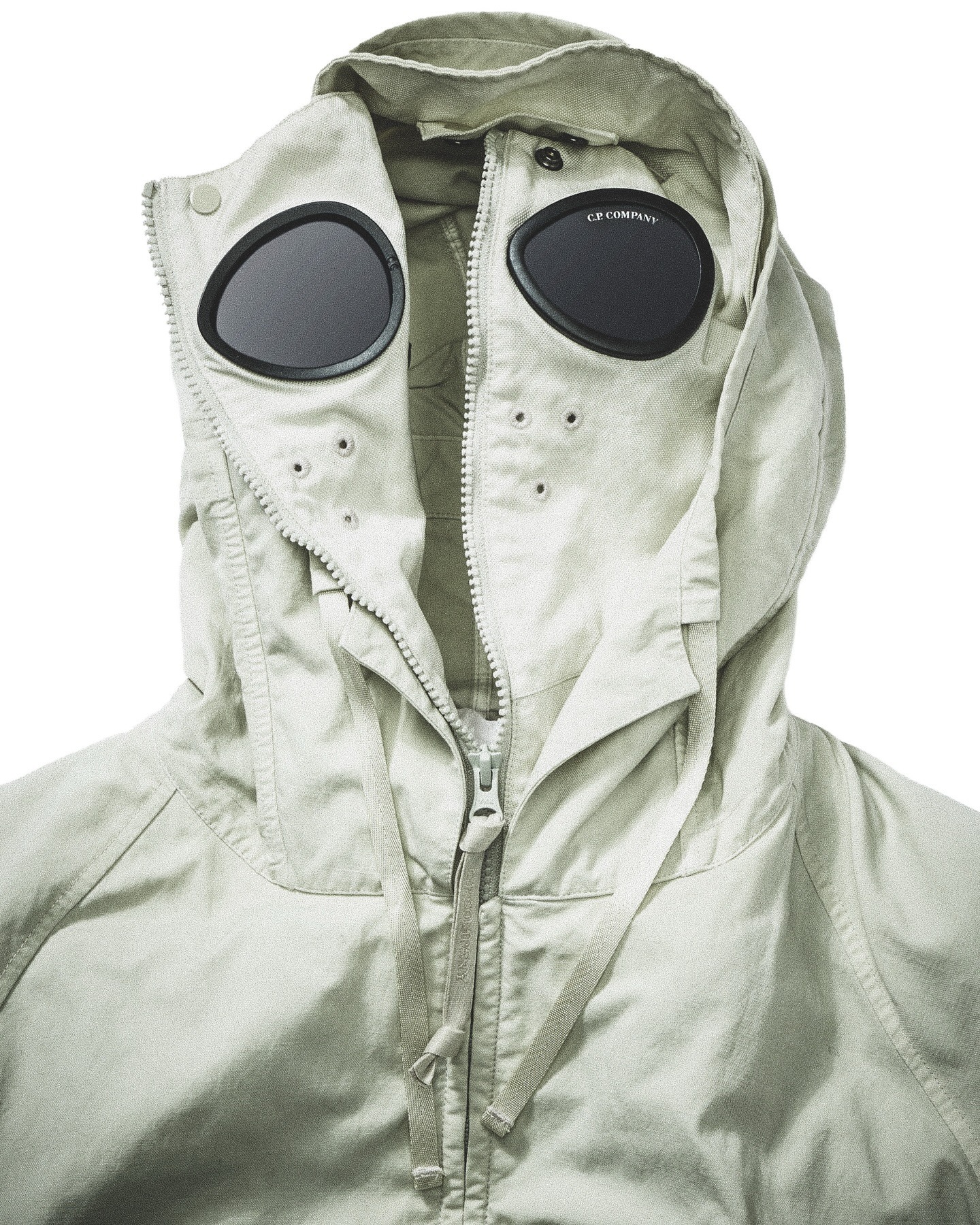 Light khaki hooded jacket with zip front and integrated round goggle lenses on the hood, C.P. Company detail