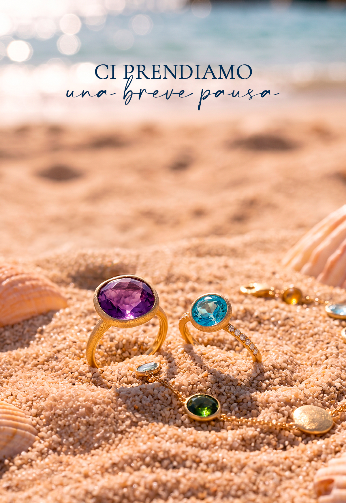 Gold rings with purple and blue gems on sunlit sandy beach with seashells, blurred sea and Italian text 'Ci prendiamo una breve pausa'