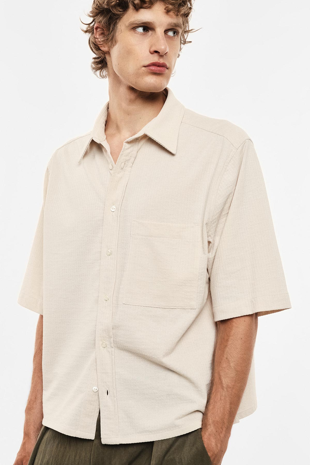Beige short-sleeve button-up shirt with chest pocket, relaxed fit on a male model looking to the right