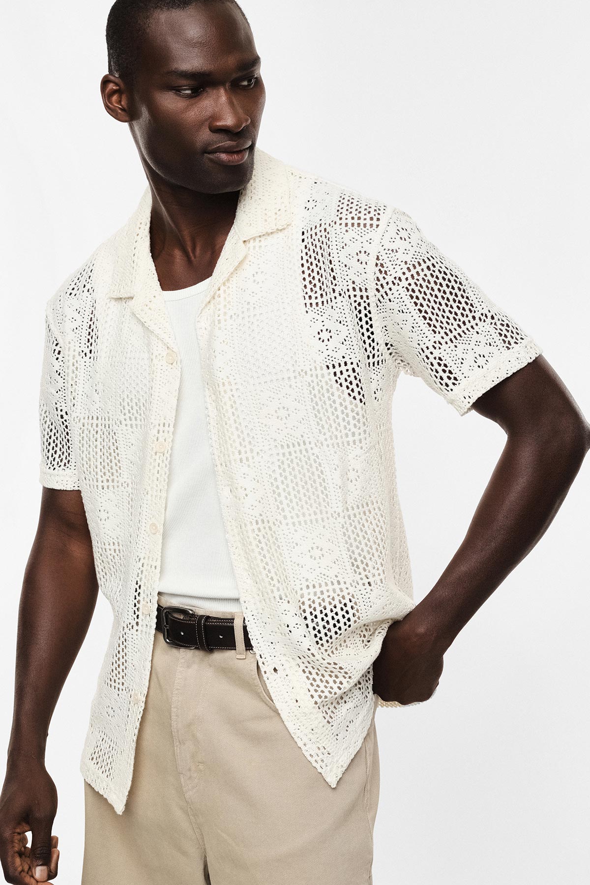 Man wearing cream crochet short-sleeve shirt over white vest, beige trousers and black belt — casual summer outfit