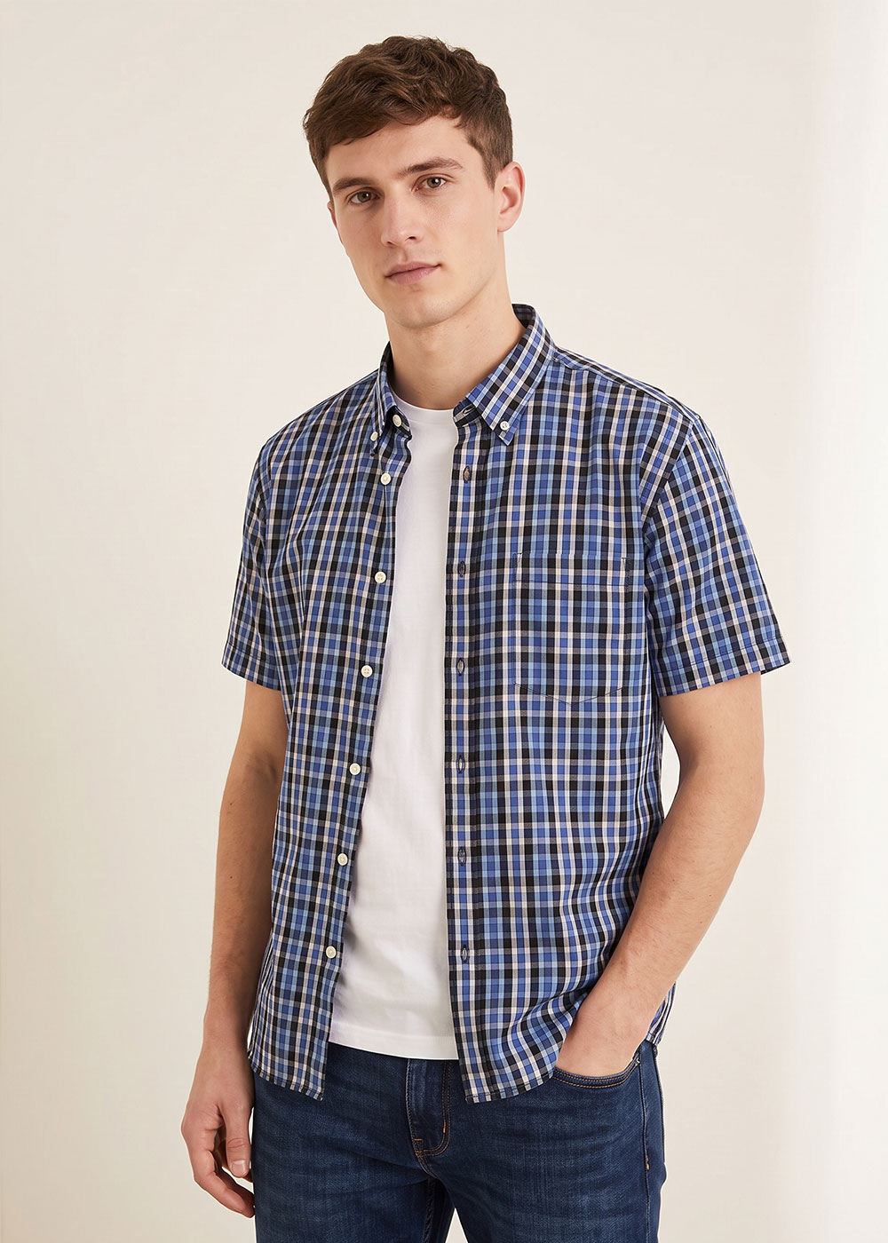 Man modelling blue check short-sleeve button-up shirt over a white T-shirt with jeans against a neutral background