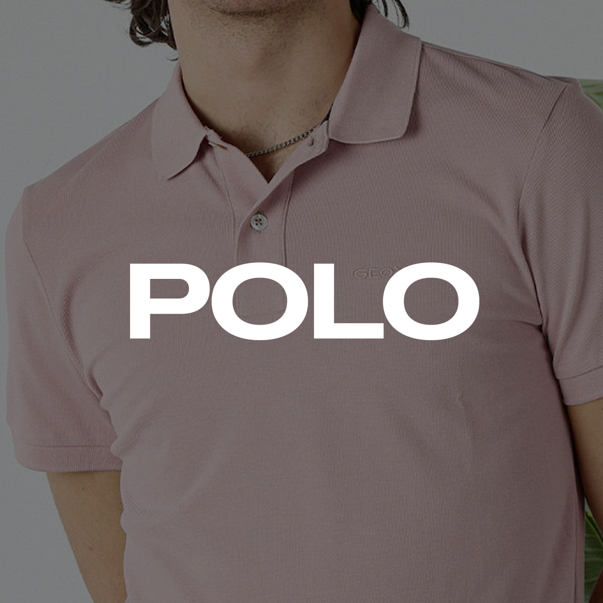 Close-up of person wearing pale pink short-sleeve polo shirt with two-button placket, subtle embroidered logo and silver chain
