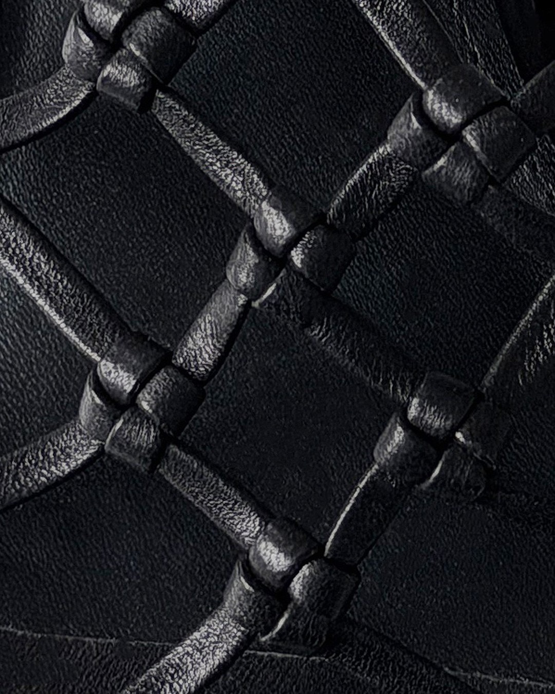 Close-up of black woven leather upholstery with knotted intersections forming a diamond quilted texture