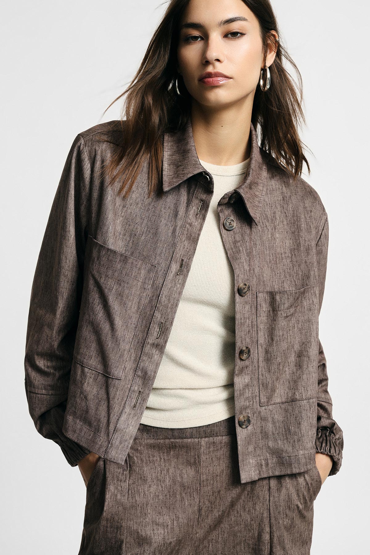 Woman wearing brown textured jacket and matching skirt over cream ribbed top, hands in pockets against a neutral studio background