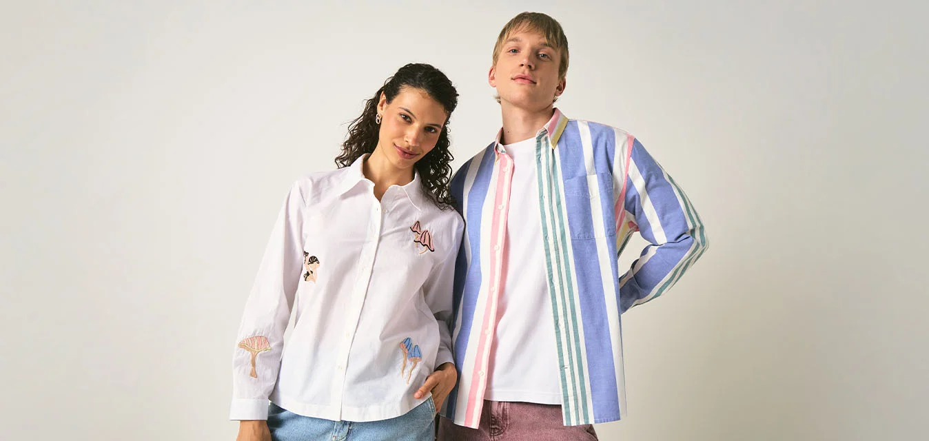 Due giovani adulti vestiti in modo informale stanno uno accanto all'altro davanti a uno sfondo chiaro e uniforme, uno indossa una camicia a righe e l'altro una camicia bianca con disegni.
