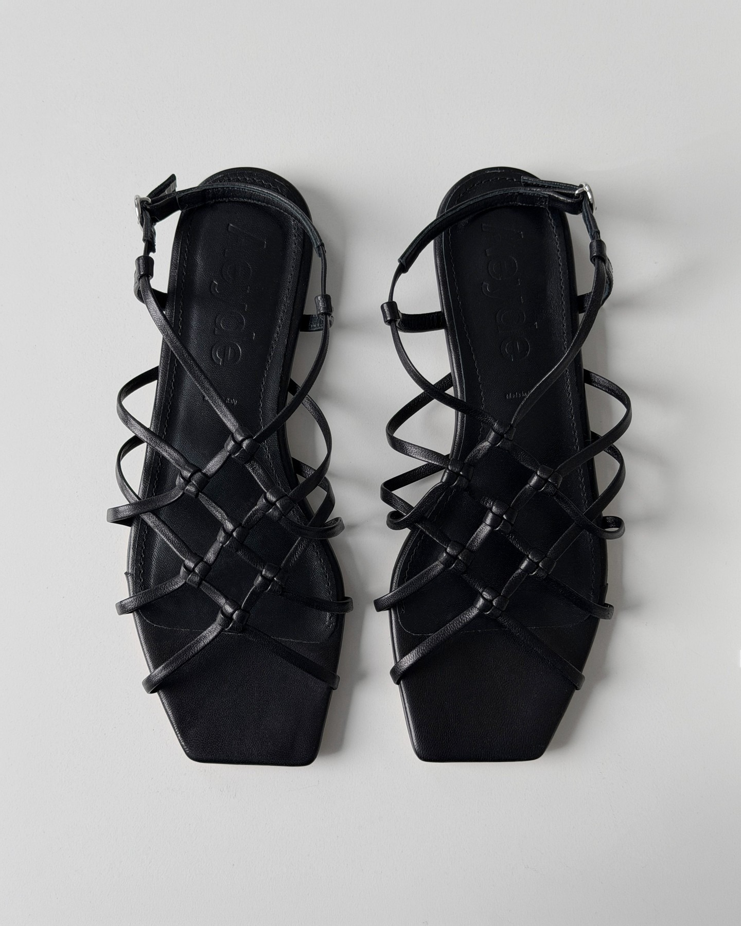 Top-down view of women's black leather strappy flat sandals with square toe on a pale background