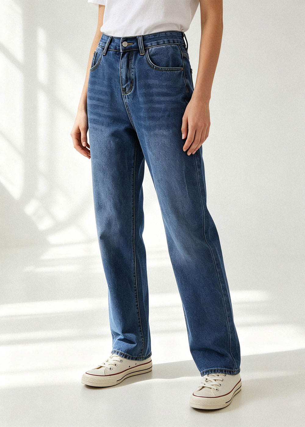 Model wearing high-waisted blue denim straight-leg jeans with white T-shirt and cream canvas trainers