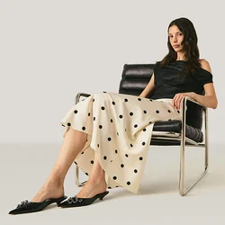Donna con top nero e gonna a pois seduta su una sedia moderna nera su uno sfondo chiaro e semplice.