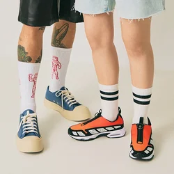 Due persone in piedi su un pavimento chiaro, una indossa pantaloni corti neri, scarpe da ginnastica blu e calzini bianchi con disegni rossi, l'altra indossa pantaloni corti in denim, scarpe da ginnastica arancioni e calzini bianchi a righe.