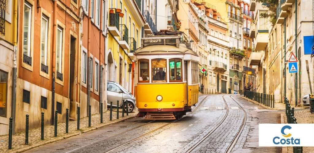 Yellow vintage tram travelling up a cobbled street lined with colourful buildings and balconies in Lisbon, Portugal
