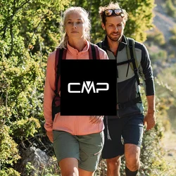 Due escursionisti con abbigliamento da esterni camminano su un sentiero sterrato accanto a un fiume, circondati da alberi verdi e colline illuminate dal sole.