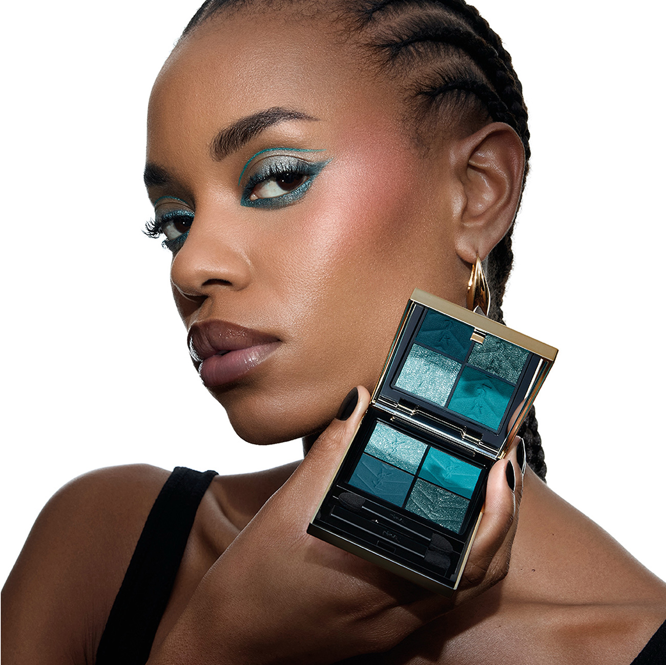 Una donna dalla pelle scura che mostra un trucco occhi grafico blu turchese mentre tiene in mano la palette YSL abbinata.