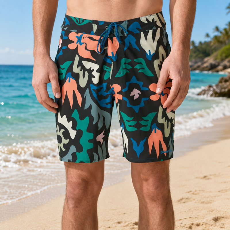 Men's colourful camo-pattern swim shorts with drawstring standing on sandy tropical beach with turquoise sea