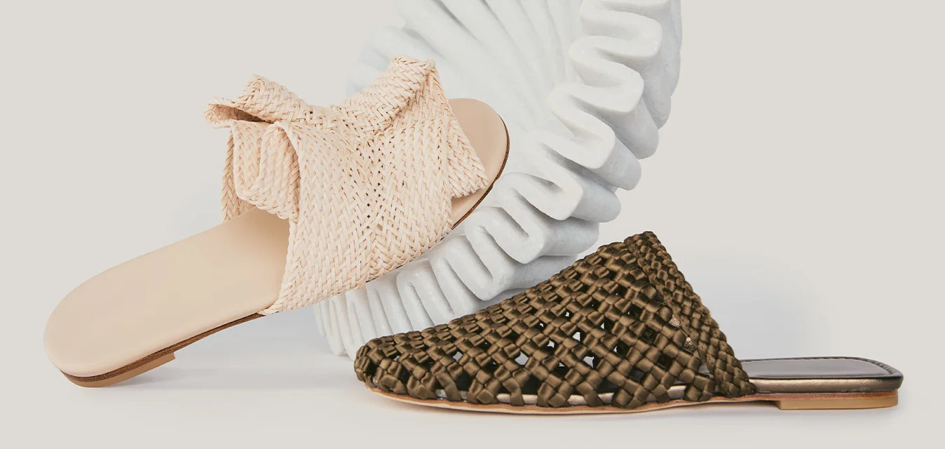 Due sandali slip-on, uno beige con tomaia in tessuto e uno marrone con design intrecciato, esposti su uno sfondo chiaro e uniforme.