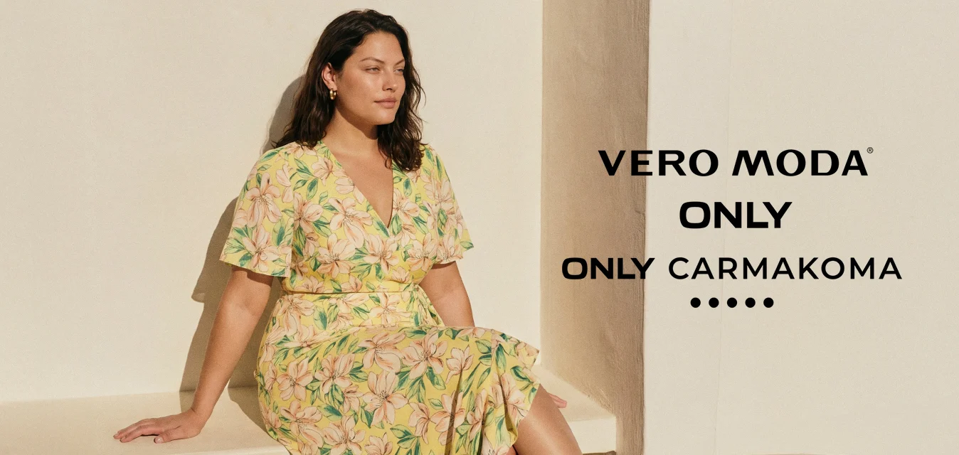 Donna con capelli scuri seduta su una panchina bianca, indossa un vestito giallo a fiori e sandali neri con tacco sotto una luce naturale intensa.