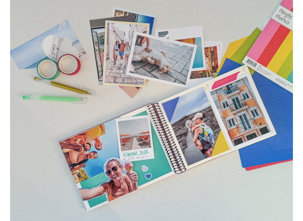 Un album aperto con foto stampate, washi tape, cartoncini colorati e adesivi per lo scrapbooking