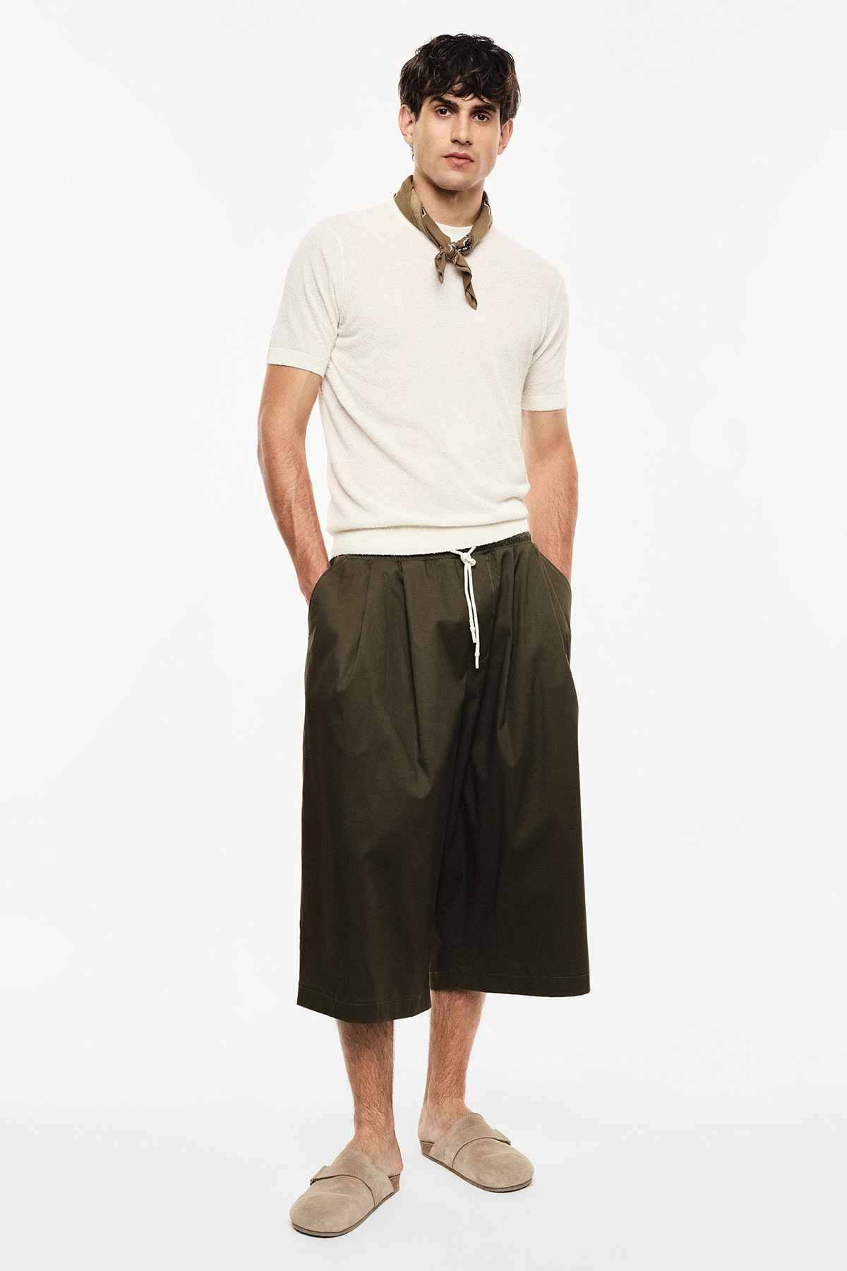 Male model in cream short-sleeve sweater, olive wide cropped trousers with drawstring, beige slip-on shoes and neckerchief
