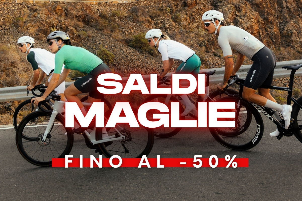 Four cyclists on road bikes ascending a mountain road; overlay reads 'Saldi Maglie fino al -50%' — up to 50% off jerseys