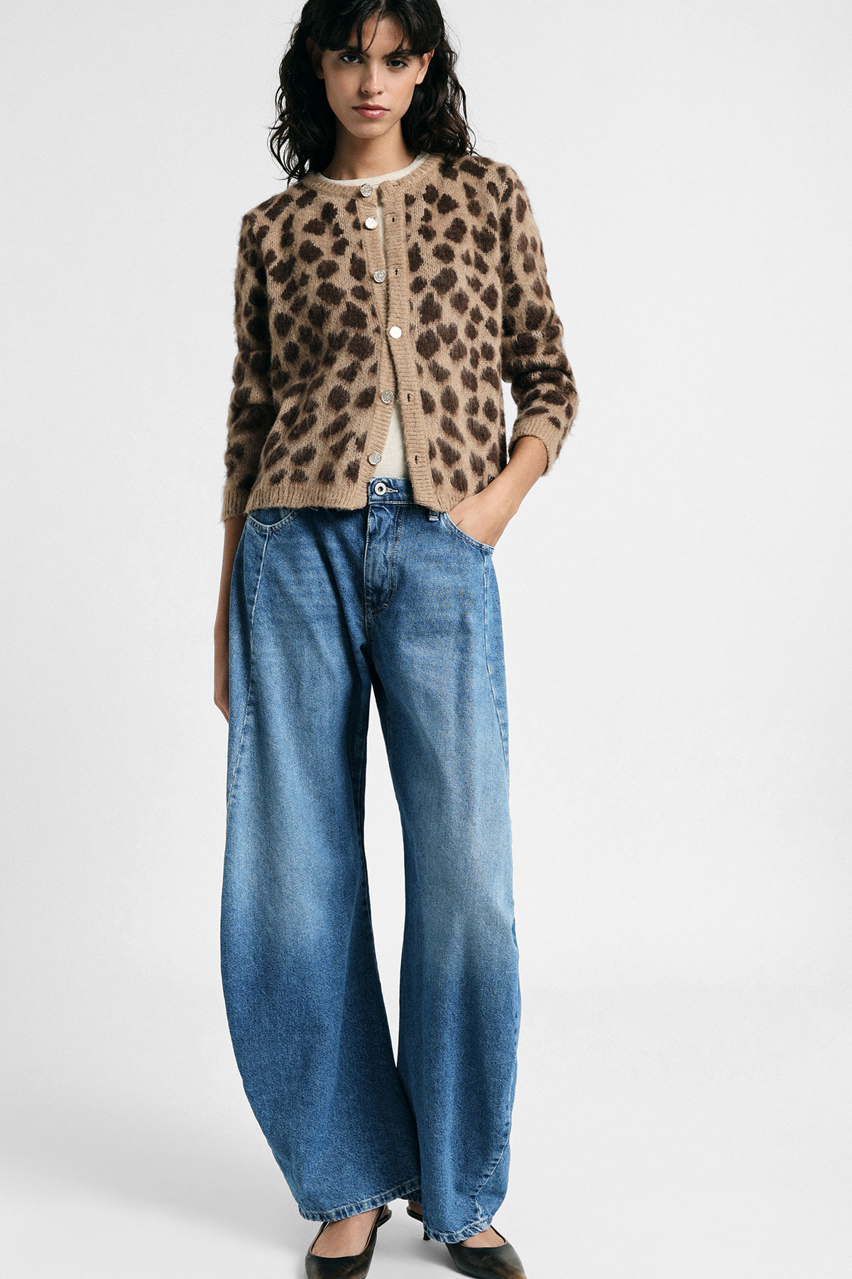 Woman model wearing a leopard-print cardigan over a beige top with wide-leg blue jeans and black heels on a plain white background