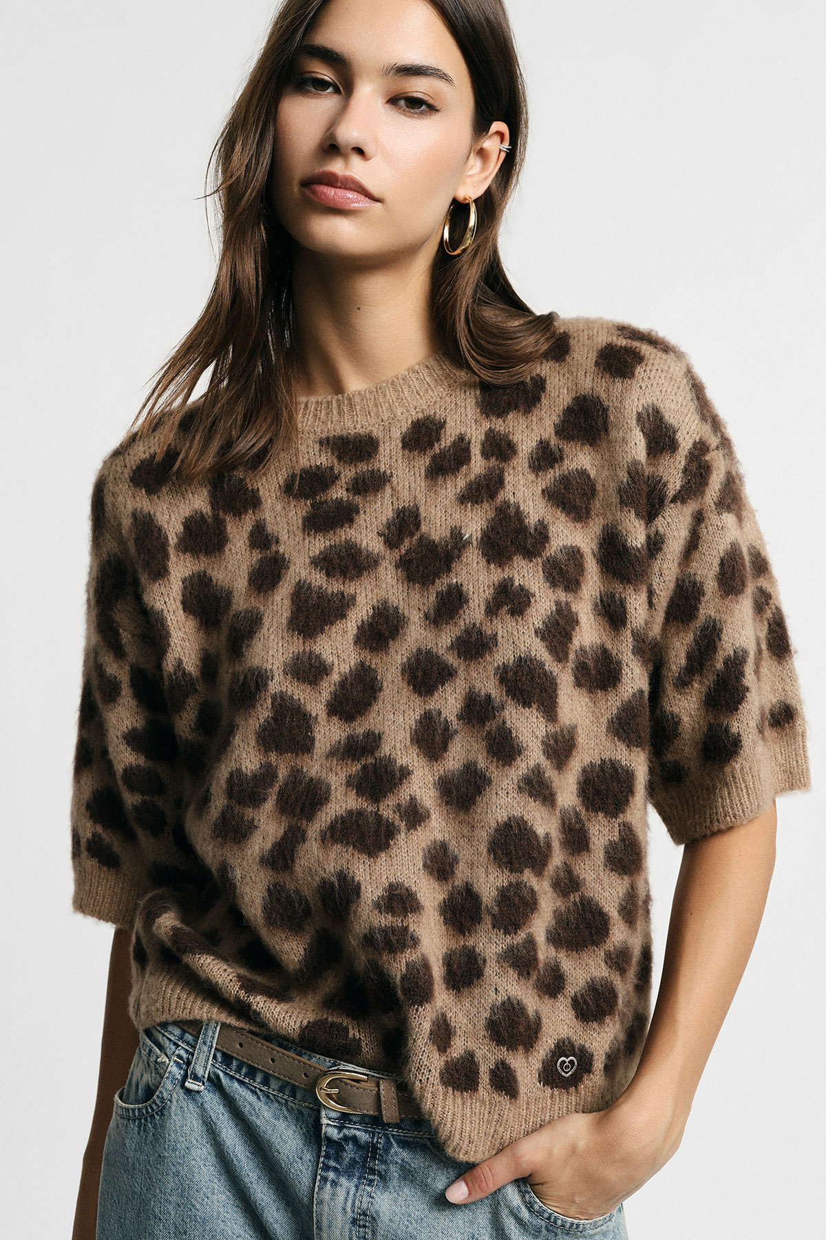 Woman wearing brown leopard-print fuzzy short-sleeve jumper with gold hoop earring, tucked into blue jeans with belt
