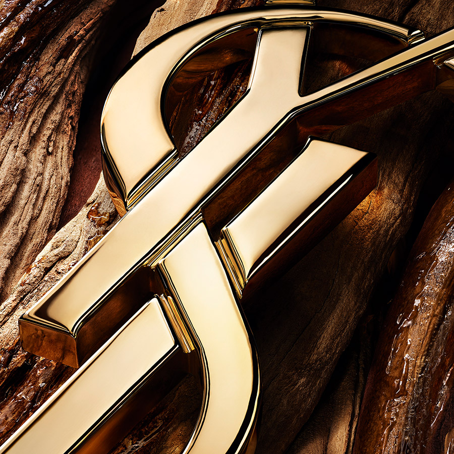 Un primo piano di un logo YSL scolpito in metallo dorato appoggiato su legno lucido dai toni caldi.