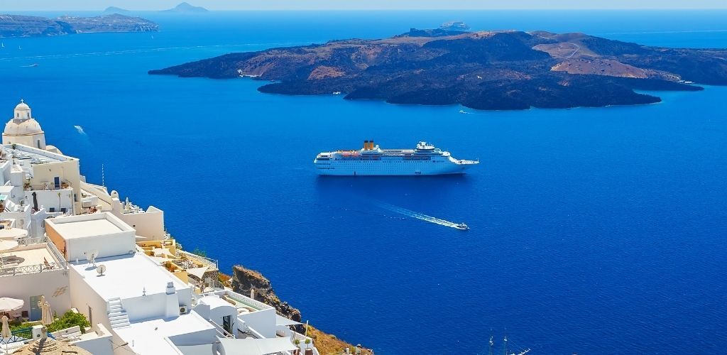 Whitewashed Santorini cliffside houses overlooking a cruise ship in the deep blue Aegean Sea and volcanic caldera