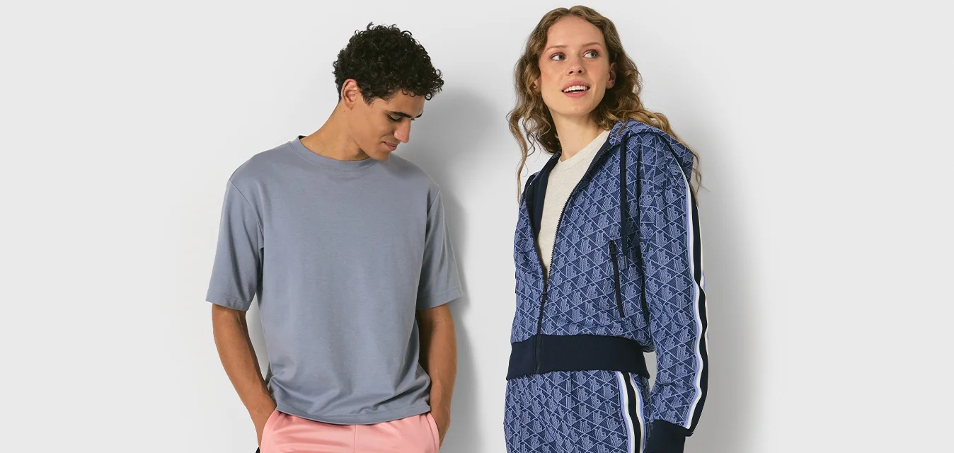 Uomo in t-shirt grigia e pantaloni rosa in piedi accanto a una donna in felpa blu con zip e pantaloni abbinati con strisce bianche.