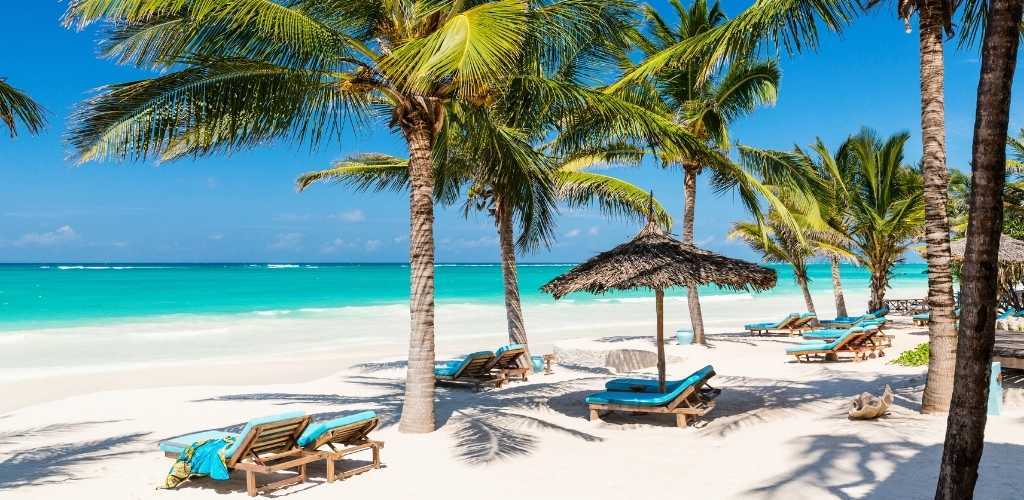 White-sand tropical beach with turquoise sea, palm trees, thatched parasols and blue-cushioned sun loungers