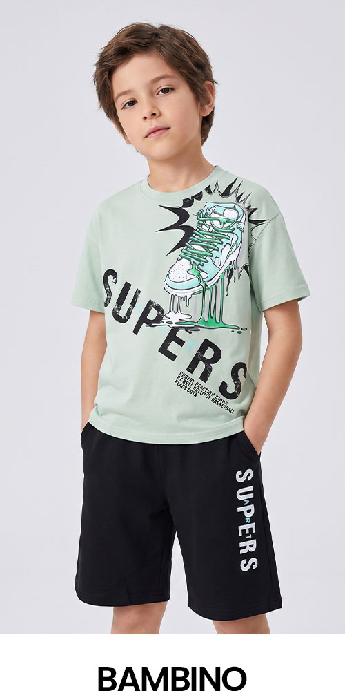 Young boy standing with hands in pockets wearing mint green T-shirt with dripping sneaker graphic and black 'SUPERS' shorts