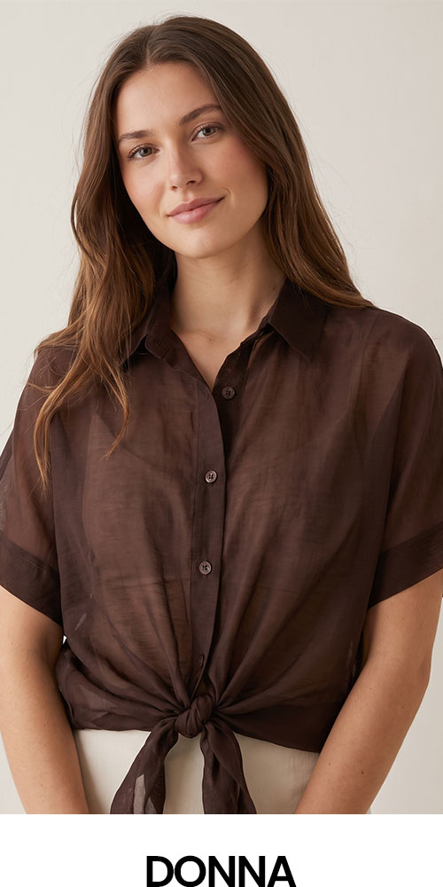 Smiling woman wearing a brown sheer short-sleeve button-up shirt tied at the waist against a neutral background