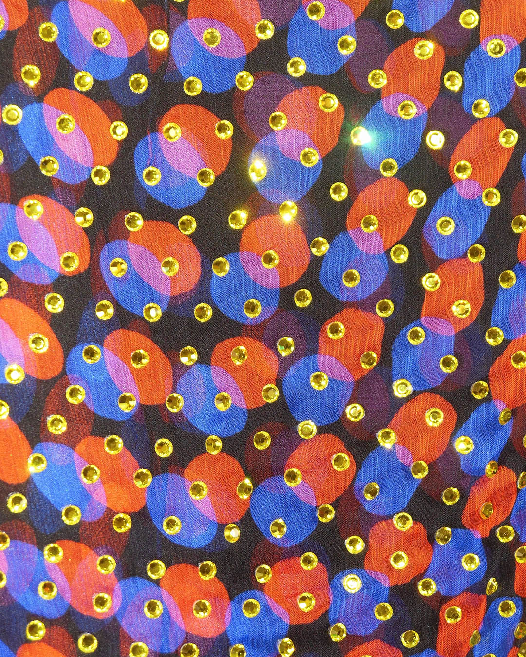 Close-up of colourful fabric with overlapping orange and blue circular pattern adorned with reflective gold sequins