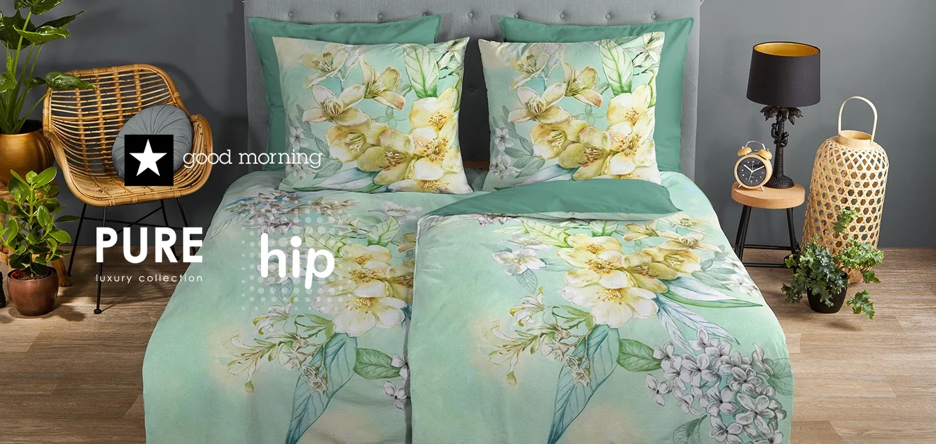 Set di copertura per il letto floreale in un delicato verde menta con motivi di fiori gialli e bianchi. Include due cuscini abbinati, presentati contro una parete grigia.