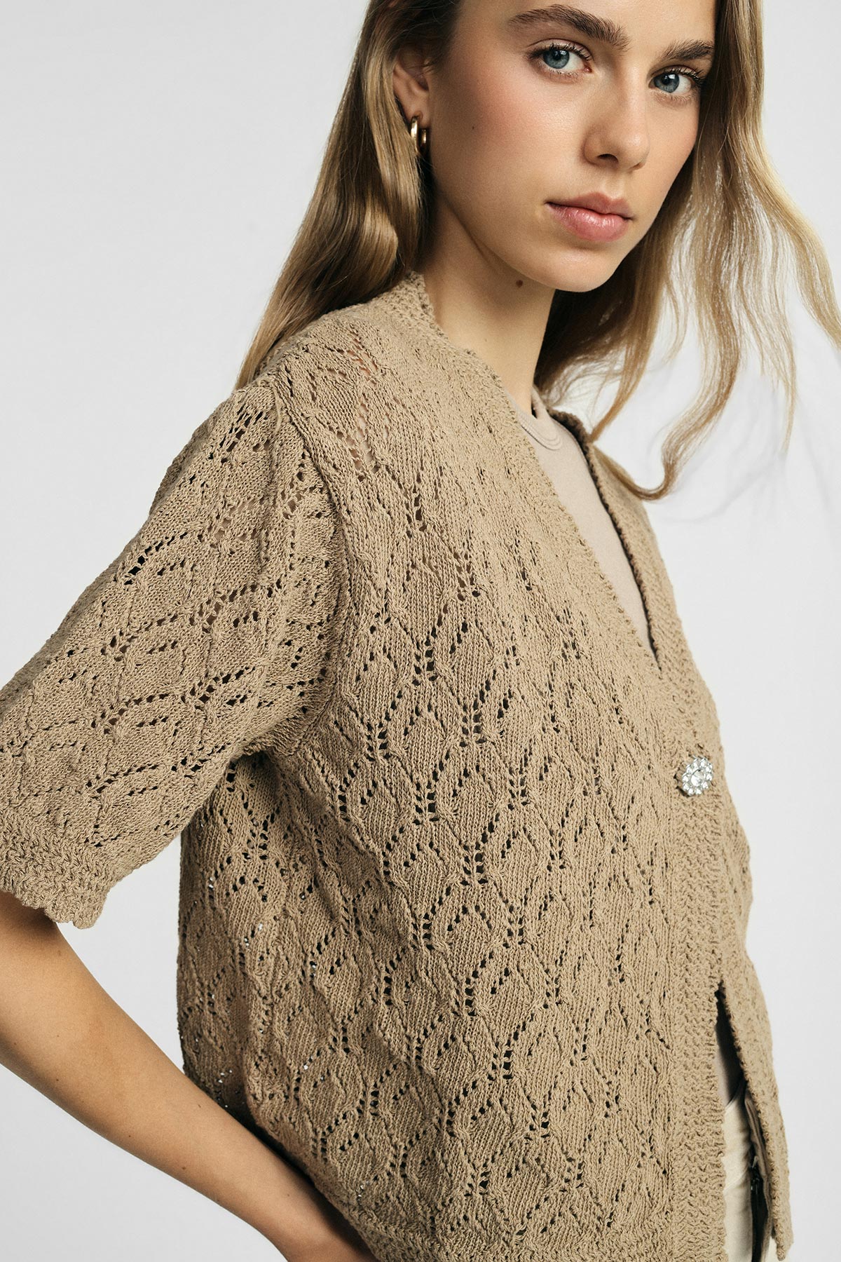 Woman wearing beige knitted short-sleeve cardigan with lacy pattern and decorative brooch, close-up